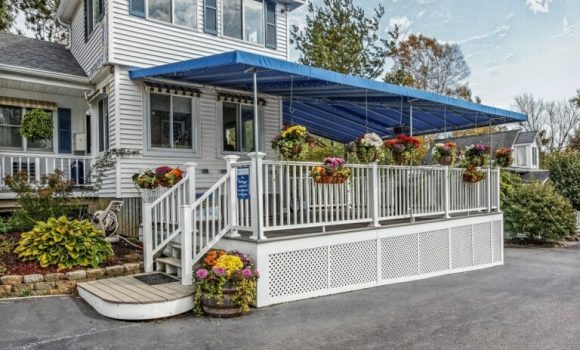 The lobby area of a midcoast Maine area motel. A blue awning shades a small front porch. Baskets of flowers hang from the awning.