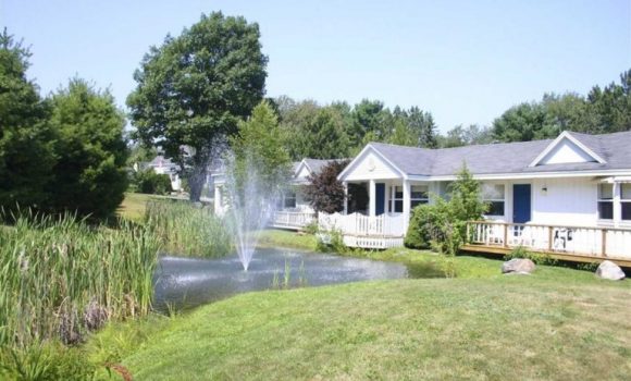 The outside view of a midcoast Maine area hotel. A fountain sprays out of a small pond lined with reeds and trees.